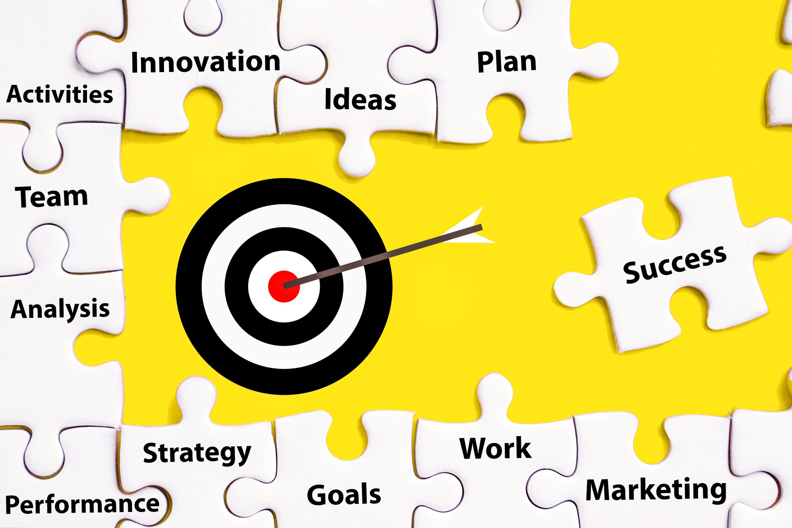 Vivid illustration of a yellow puzzle with pieces labeled 'Innovation,' 'Team,' 'Analysis,' 'Strategy,' 'Goals,' 'Work,' 'Marketing,' and 'Success' surrounding a central target with a dart in the bullseye, symbolizing the precise achievement of business objectives.