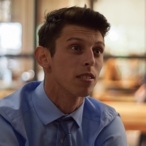 Photo of Christian Barry, Co-Founder & Chief Strategy Officer, wearing a blue shirt and tie, looking attentively during a meeting.